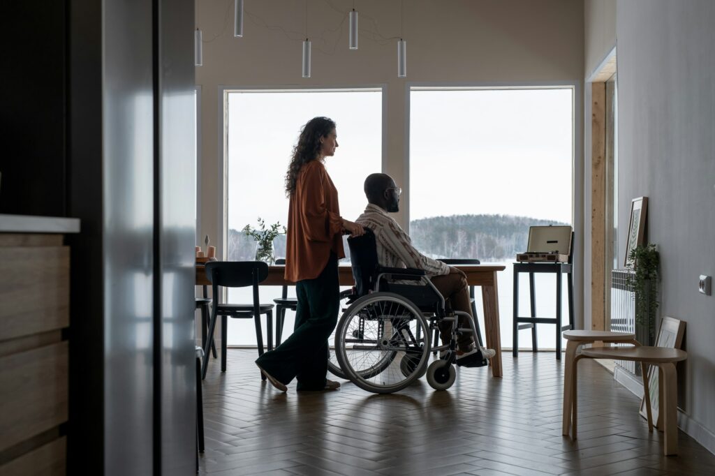 Side view of young female caregiver pushing wheelchair with African American man