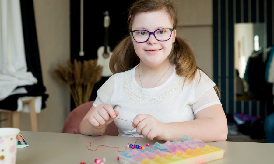 teen girl stringing beads and making bracelet. Down syndrome kid crafting jewelry and threading bead